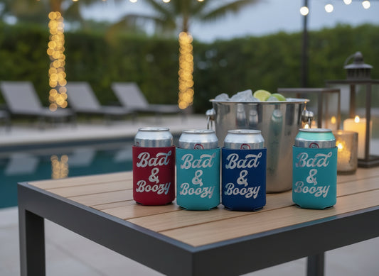 Four can coolers with 'Bad & Boozy' text on a wooden surface